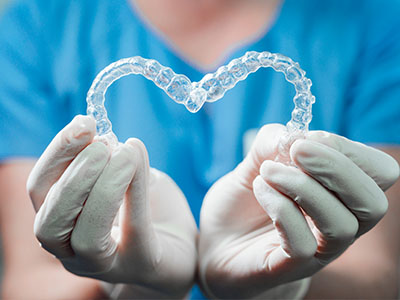 A dental professional holding a heart-shaped transparent orthodontic appliance, symbolizing love and care for oral health.