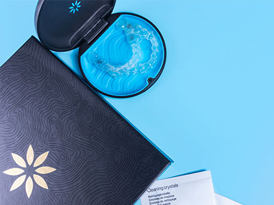 A blue toothbrush in a holder next to an open box with a floral design and a small cardboard package, all set against a blue background.