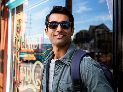 A man in sunglasses, standing outdoors and wearing a backpack, poses confidently for the camera.